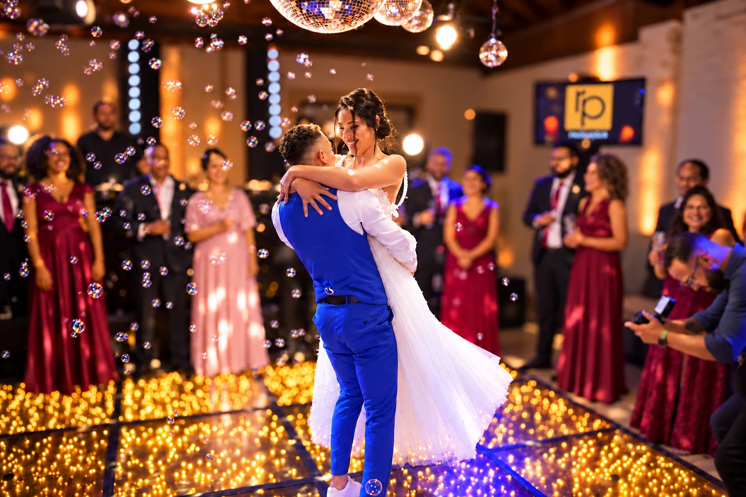 Casal dançando em uma pista iluminada, cercado por convidados e bolhas.